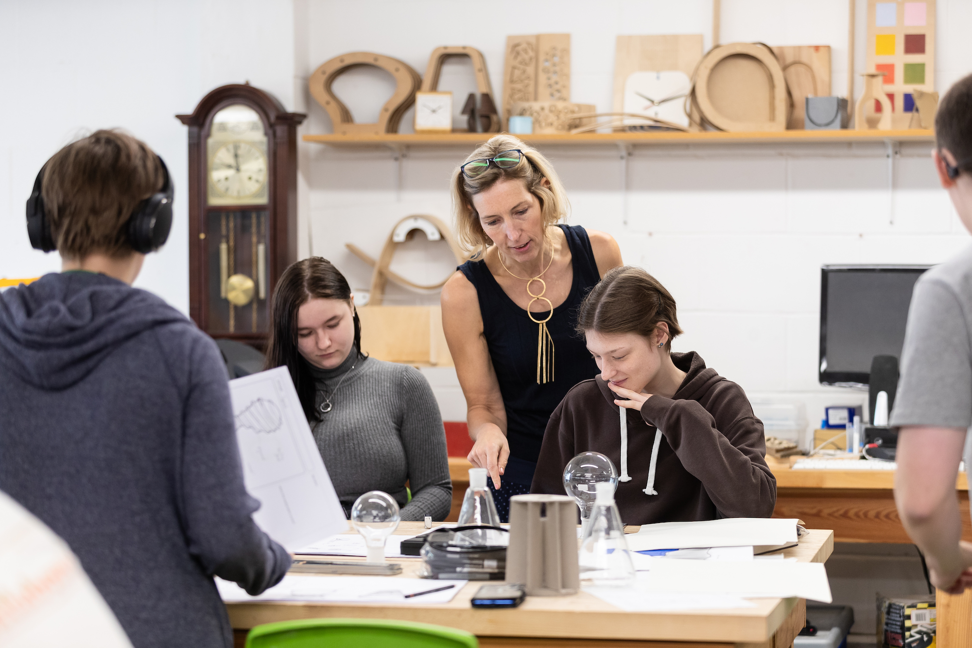 two students sitting at a workstation and a lecturer standing between them, looking at their work in art and design studio