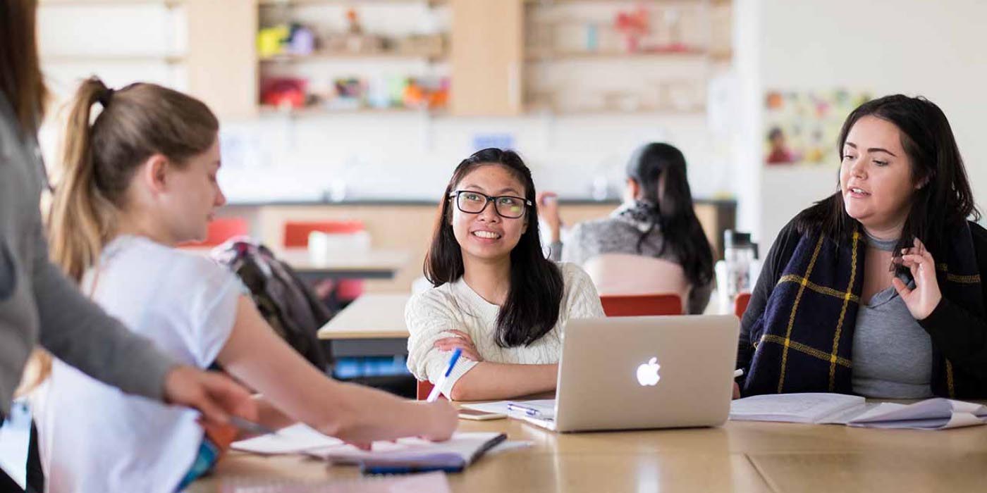 A group of female teacher training students around table writing notes and open laptop screen.