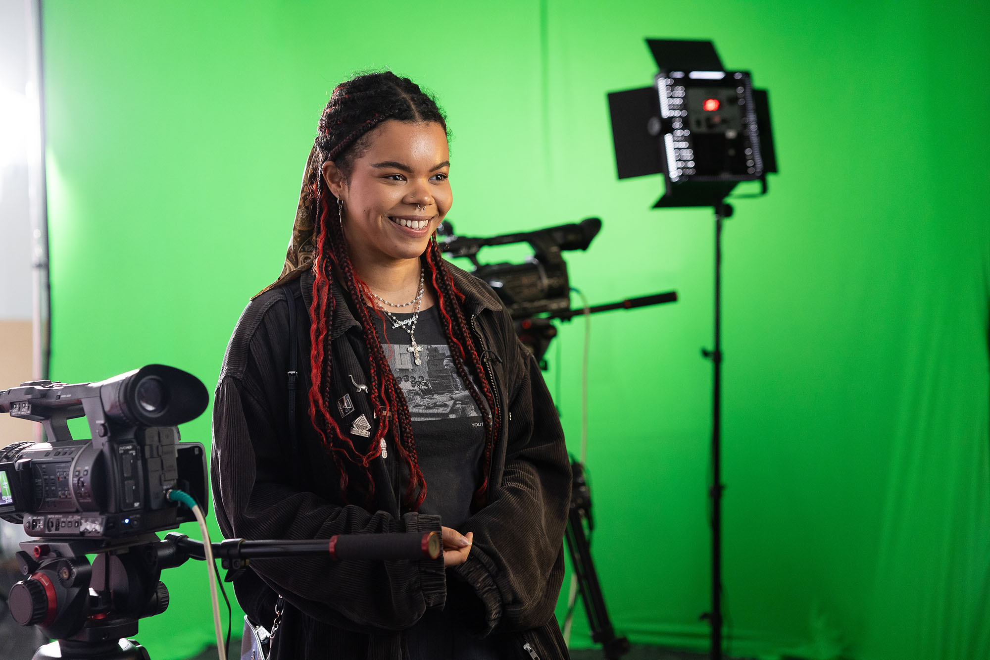 Student smiling at camera while standing in front of green screen.