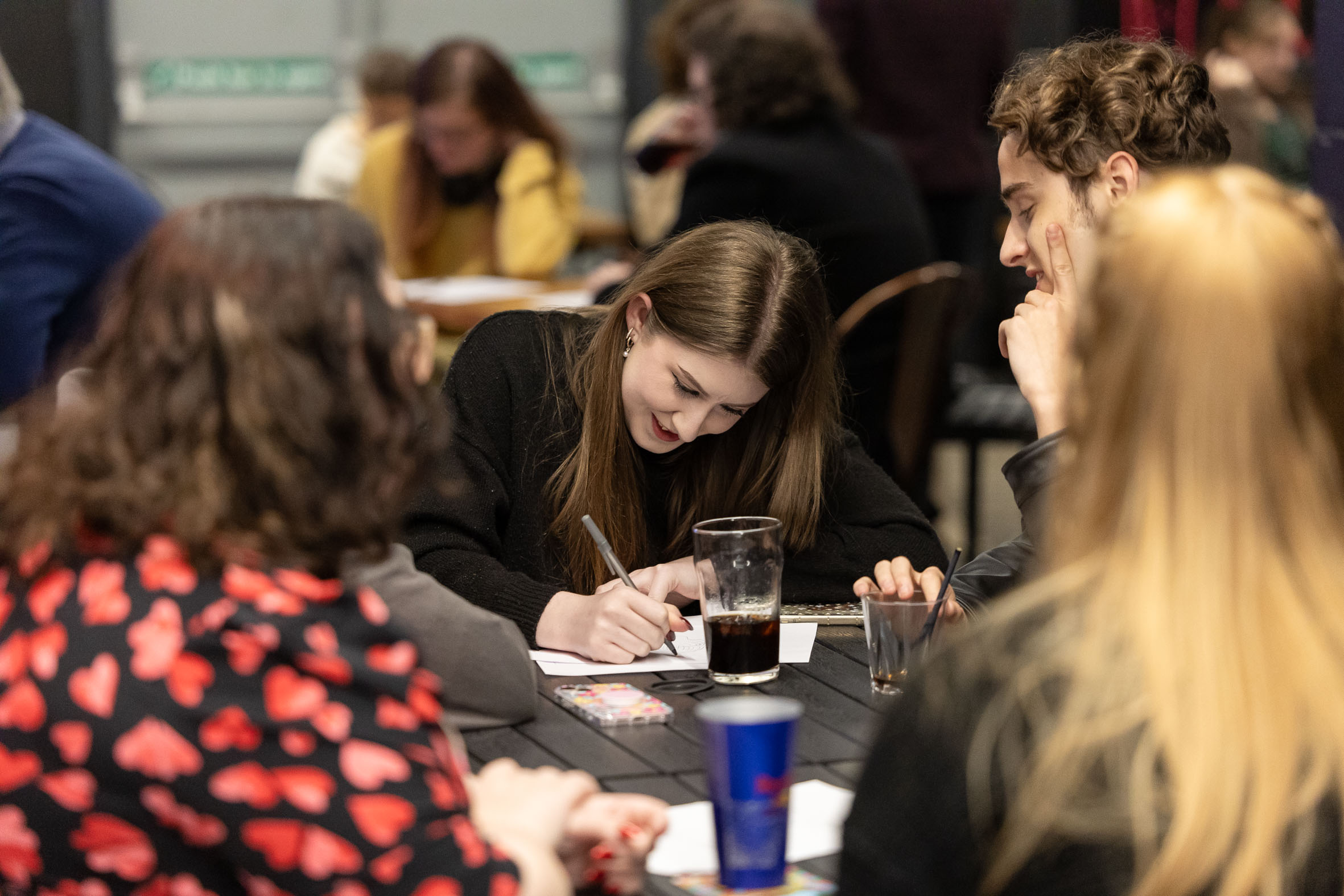 Students having drinks and writing down answers at MIFM charity pub quiz